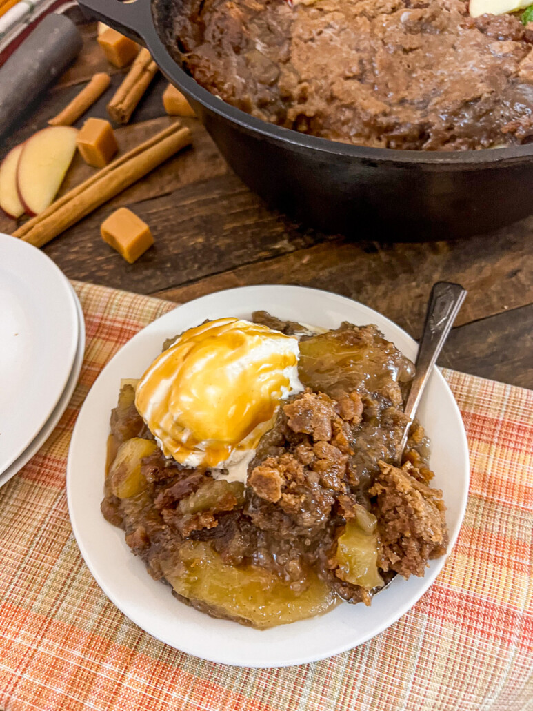 A hearty serving of caramel apple cake with a scoop of vanilla ice cream and caramel sauce.