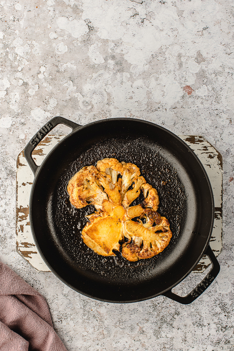 A slice of cauliflower steak on a skillet.
