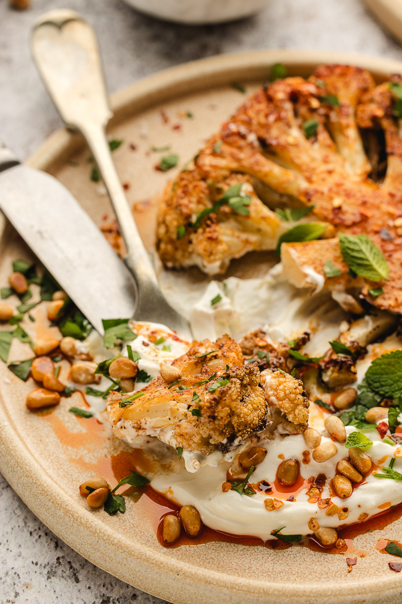 A fork picking up a piece of cauliflower with yogurt sauce.