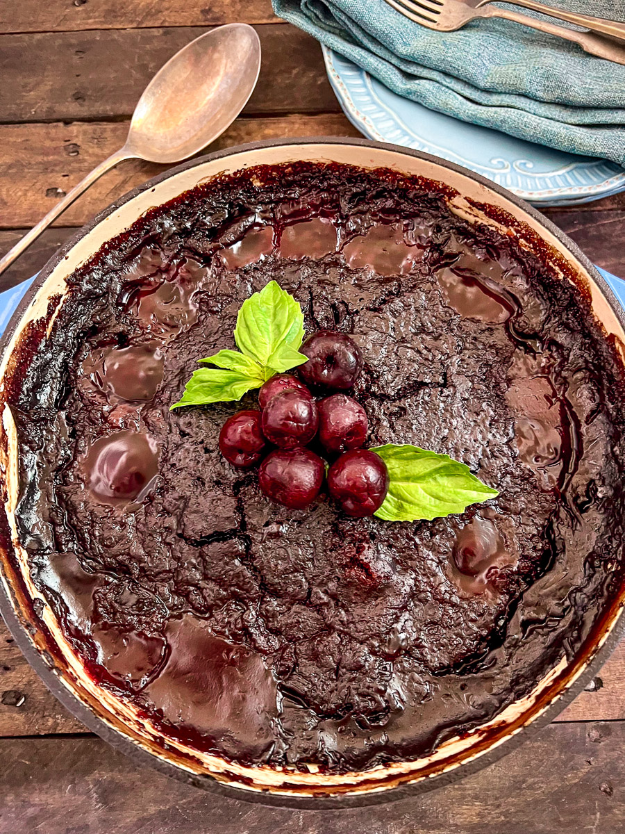 Cola Chocolate Cherry Cake in a dutch oven garnished with fresh cherries and mint leaves.