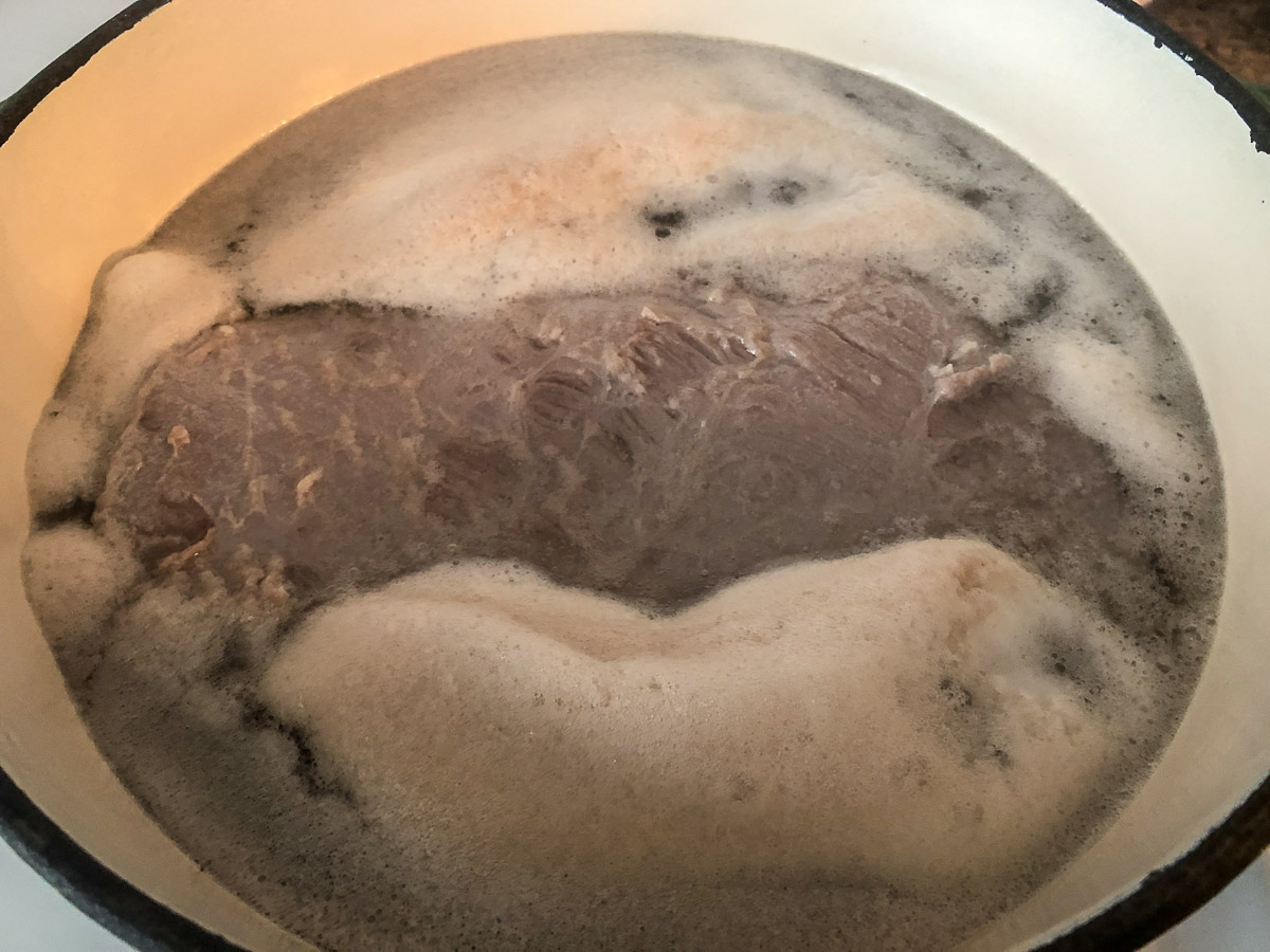 Boiling corned beef in water with foam rising to the top.