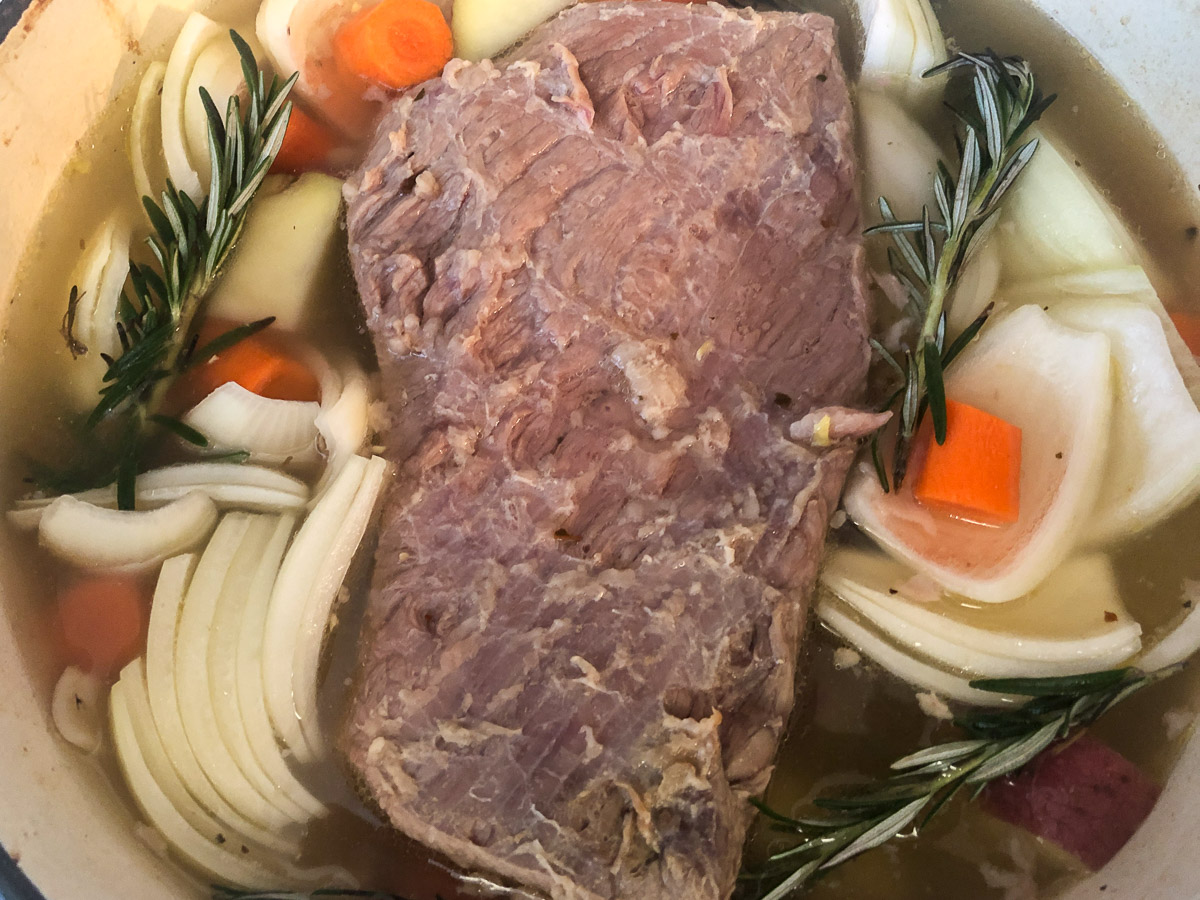 Onions, carrots, potatoes, and rosemary added to the seasoned pot of corned beef.