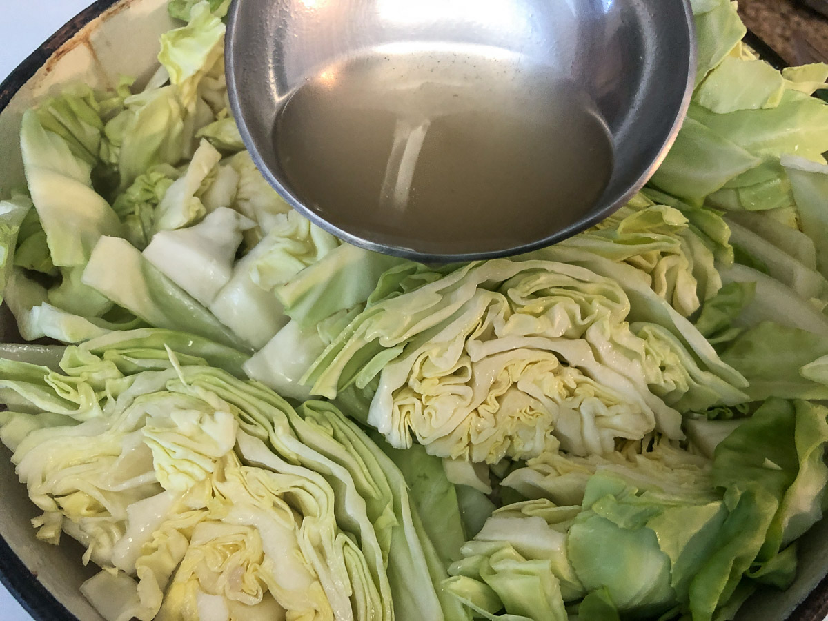 Pouring broth over the top of the cabbage.