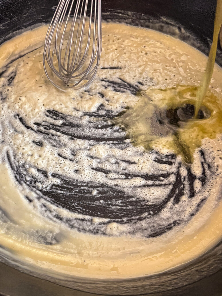 Pan drippings being poured and whisked into the roux.