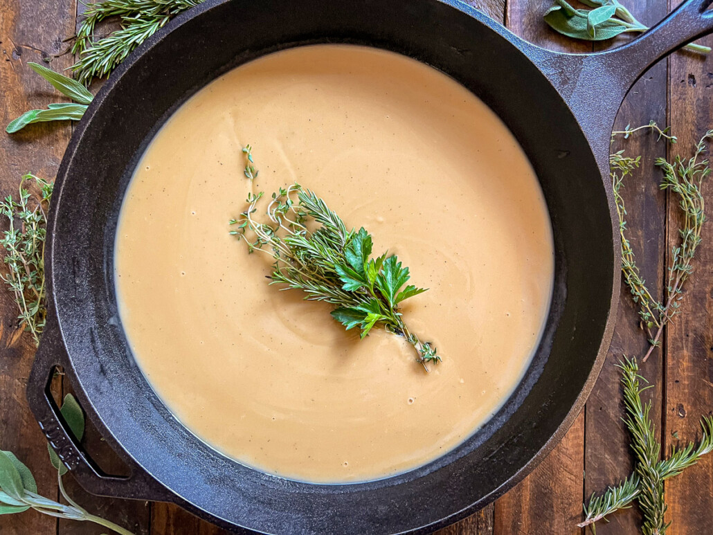 Turkey gravy cooked and garnished with a bouquet of fresh herbs in a cast iron skillet.