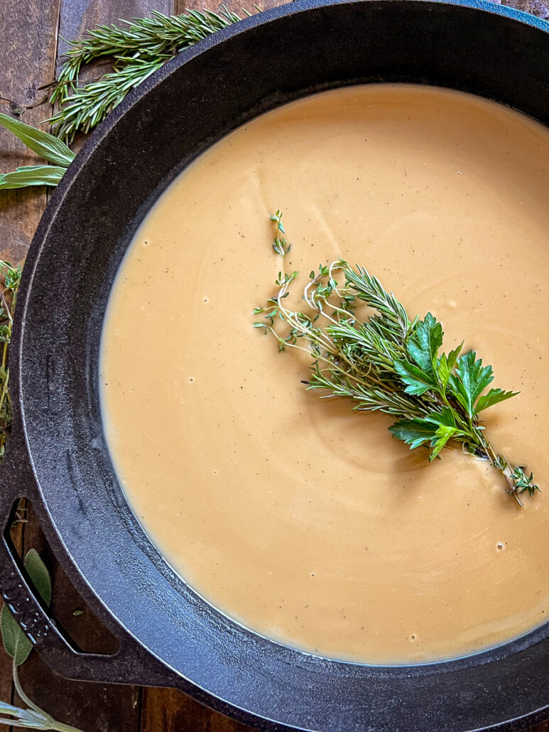 Turkey Gravy in a cast iron skillet with a bouquet of herbs as a garnish.