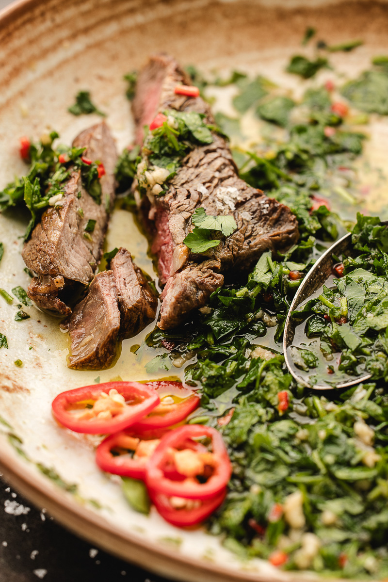 A steak cut up with chimichurri sauce spooned over it.