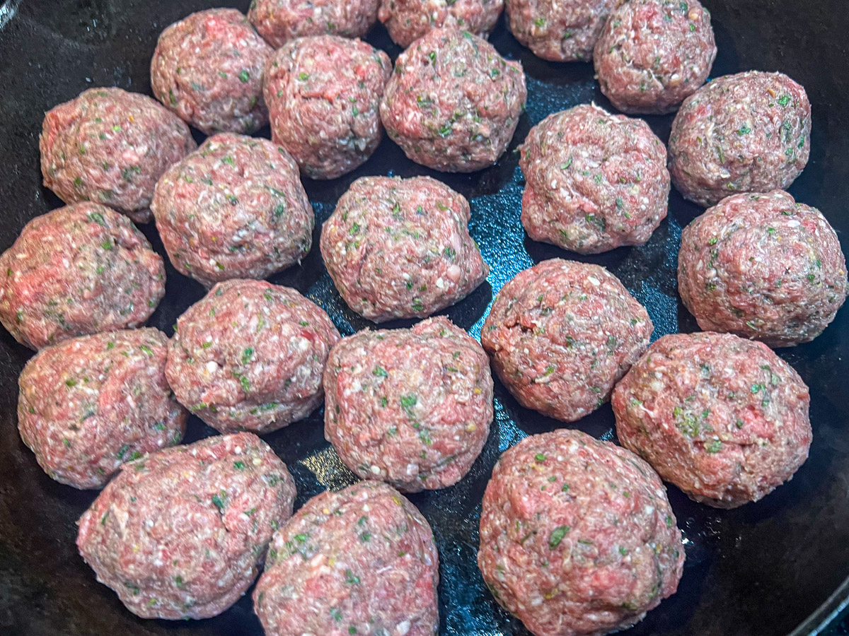 Meatballs shaped and in a cast iron skillet.