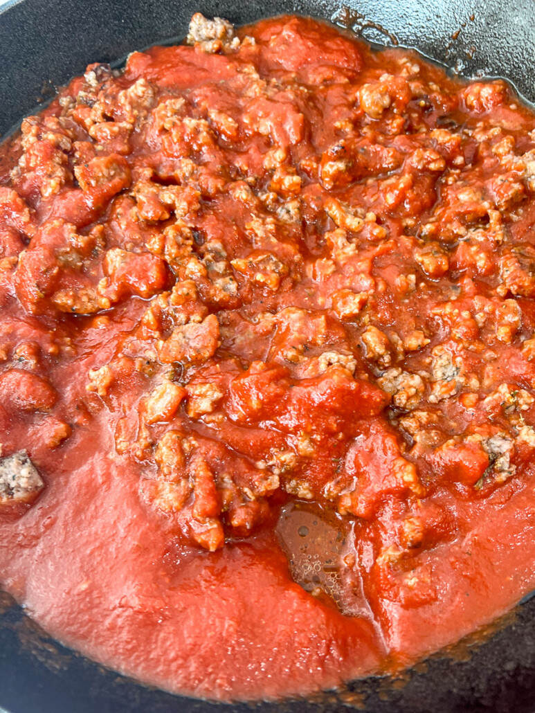 Marinara sauce has been added to the seasoned Italian sausage in the cast iron skillet.