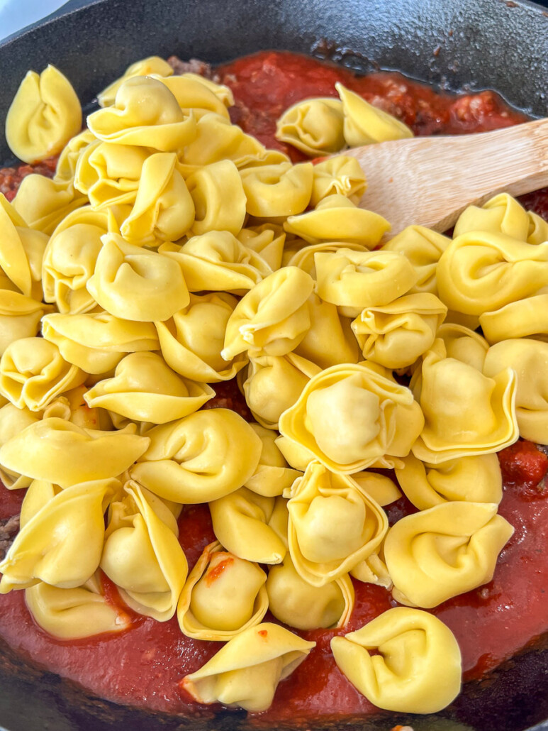 Cheese tortellini being stirred into the meat sauce.