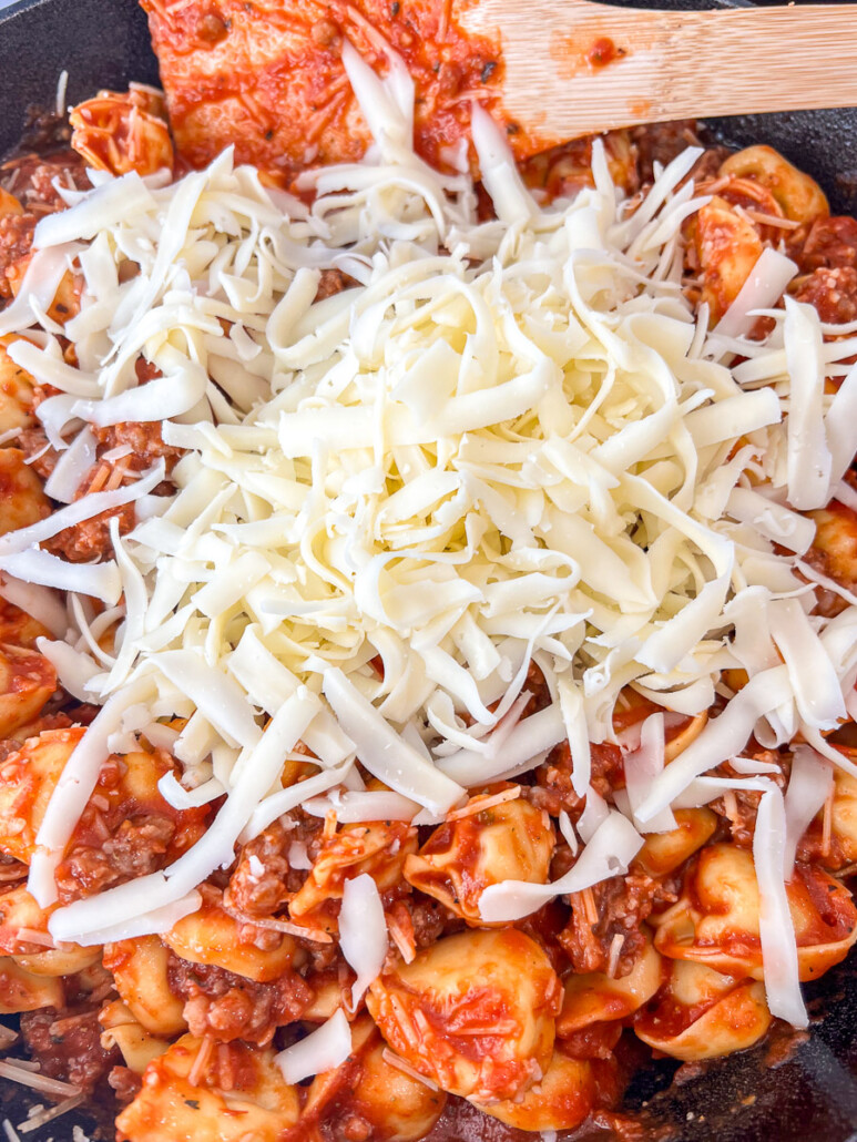Parmesan and mozzarella cheeses being stirred into the sauce and pasta mixture.