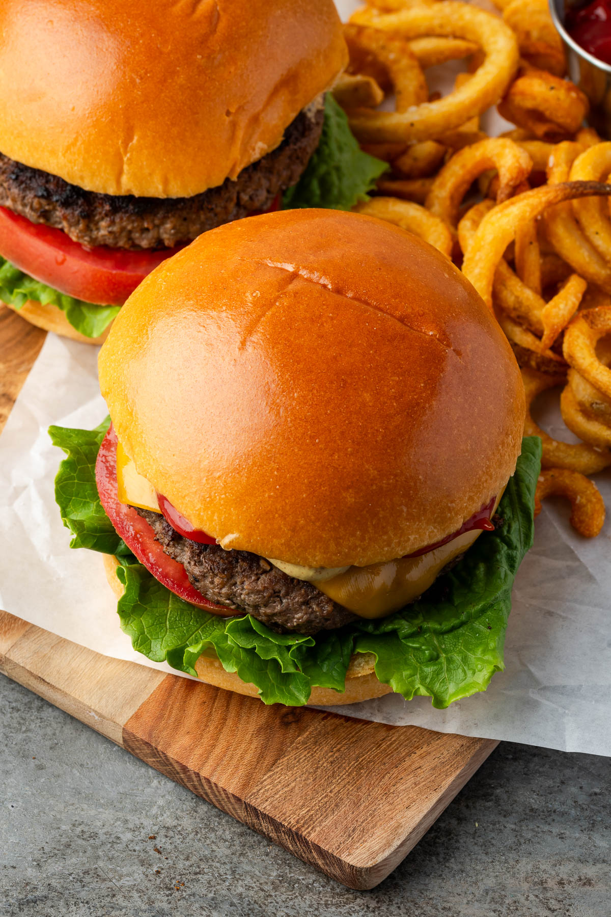 Bison burgers with lettuce, tomatoes and cheese on a wooden board.
