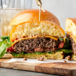 Bison burgers on a piece of parchment on a wooden board with one cut in half.