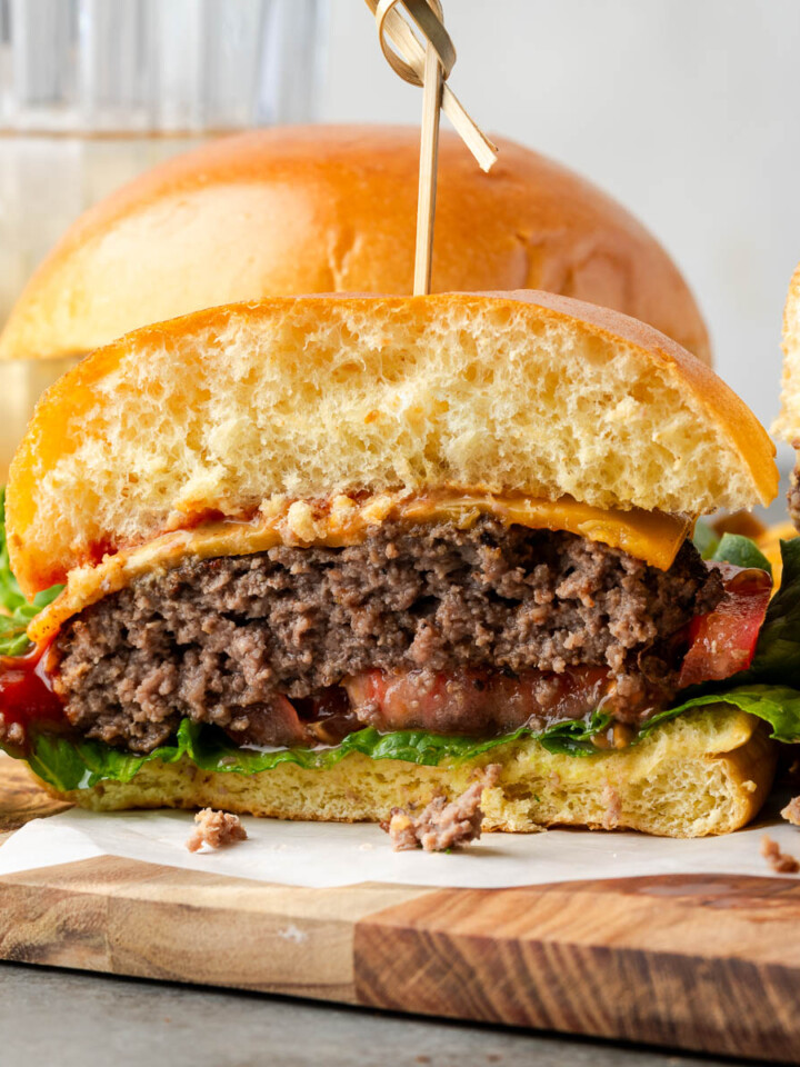 Bison burgers on a piece of parchment on a wooden board with one cut in half.