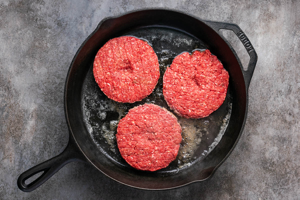 Formed bison burger patties on a hot skillet cooking.