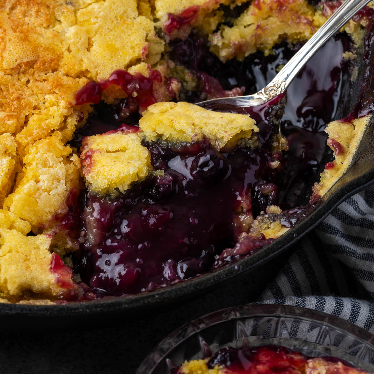 A cast iron Dutch oven with a serving of lemon blueberry dump cake scooped out.