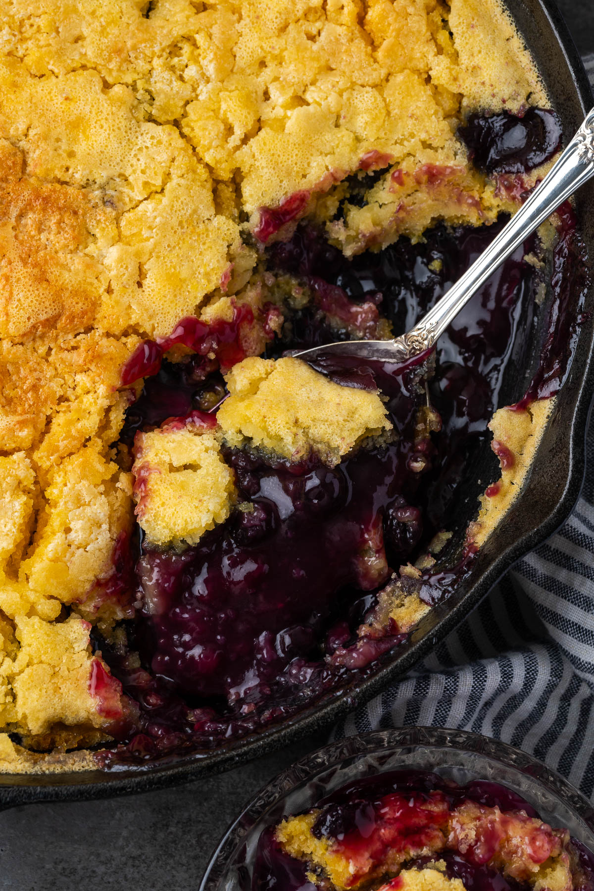 A dish of blueberry lemon dump cake in a skillet with some scooped out.
