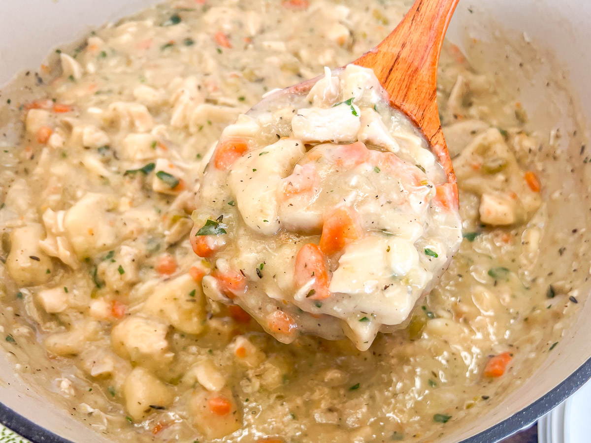 A wooden spoon scooping up some Southern chicken and dumplings from the pot.