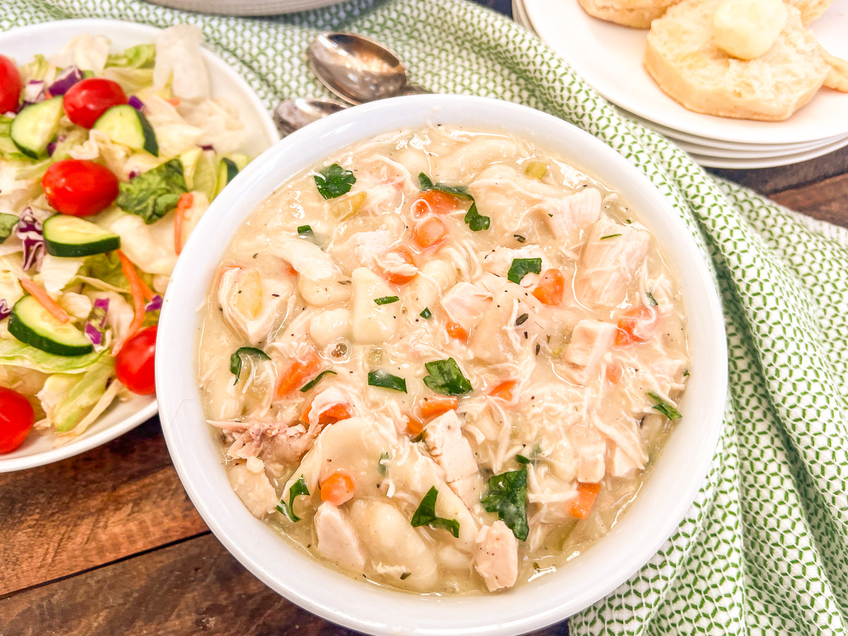 A bowl of Dutch oven chicken and dumplings on a table next to a salad.