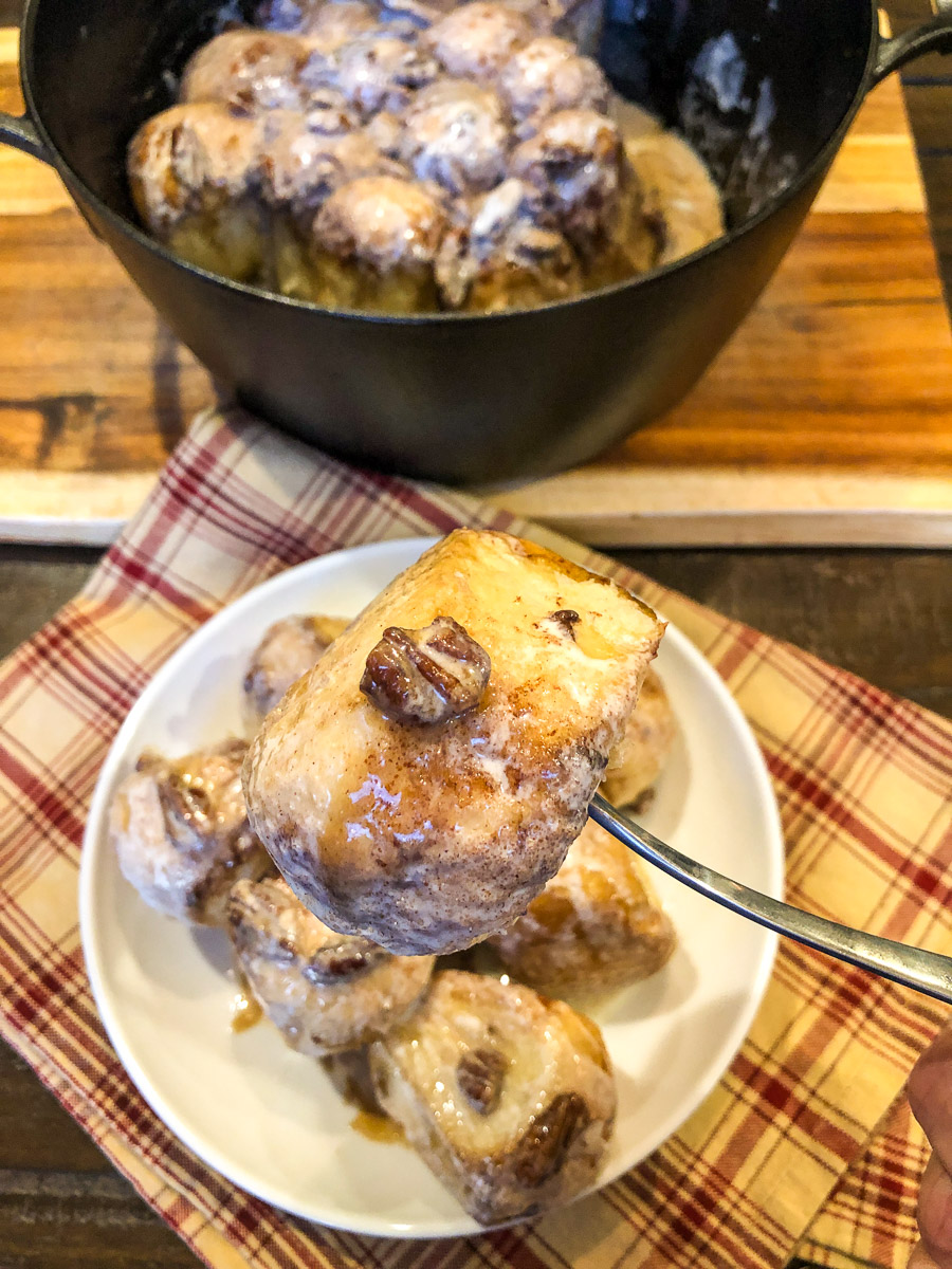 A fork hold up a piece of Dutch oven cinnamon roll in the air.