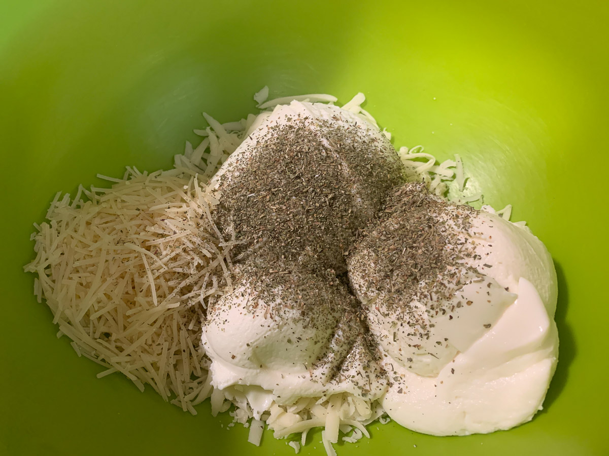 Cheeses and seasonings added to a bowl.