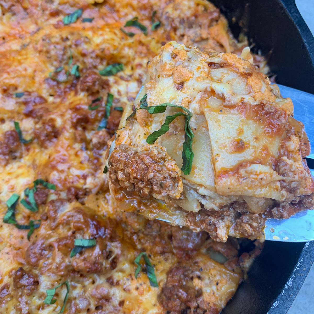 A spatula lifting up a piece of Dutch oven lasagna.