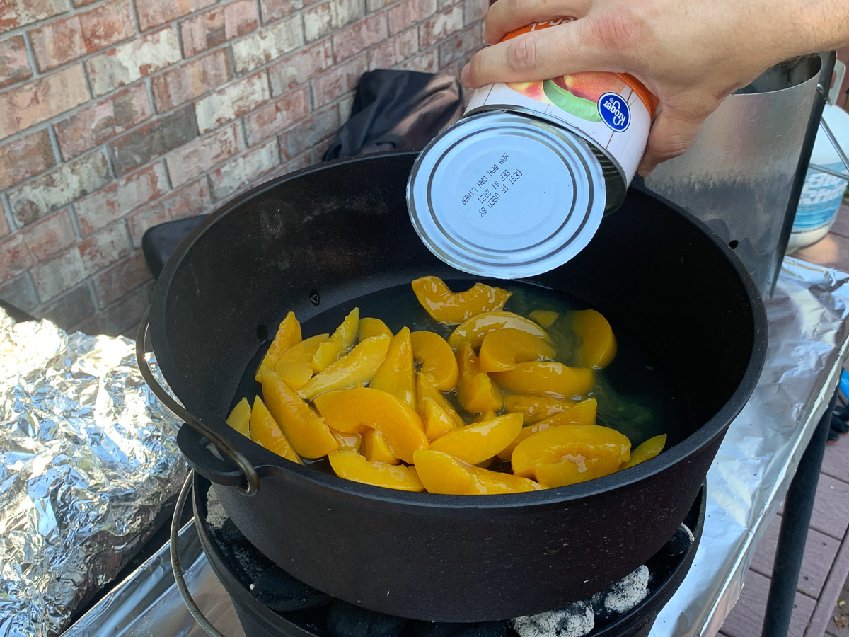 A can of peaches being dumped into a camp oven.