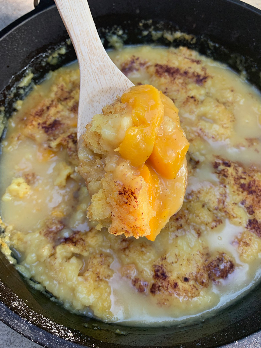 Peach dump cake with a wooden spoon lifting up a serving.