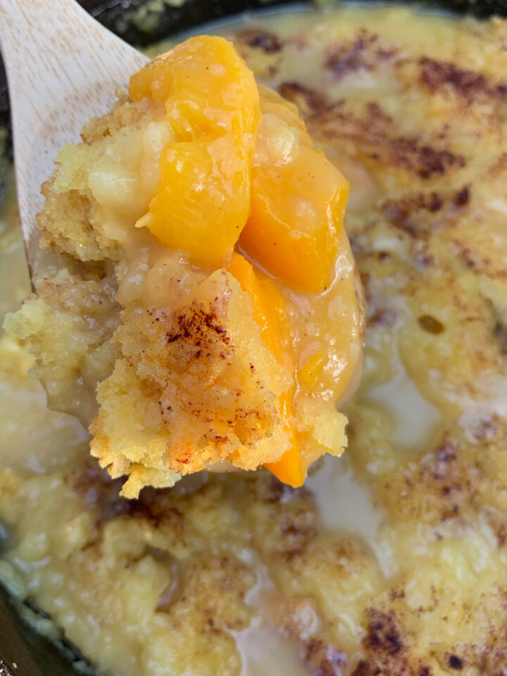 A peach dump cake with a wooden spoon lifting up a serving.