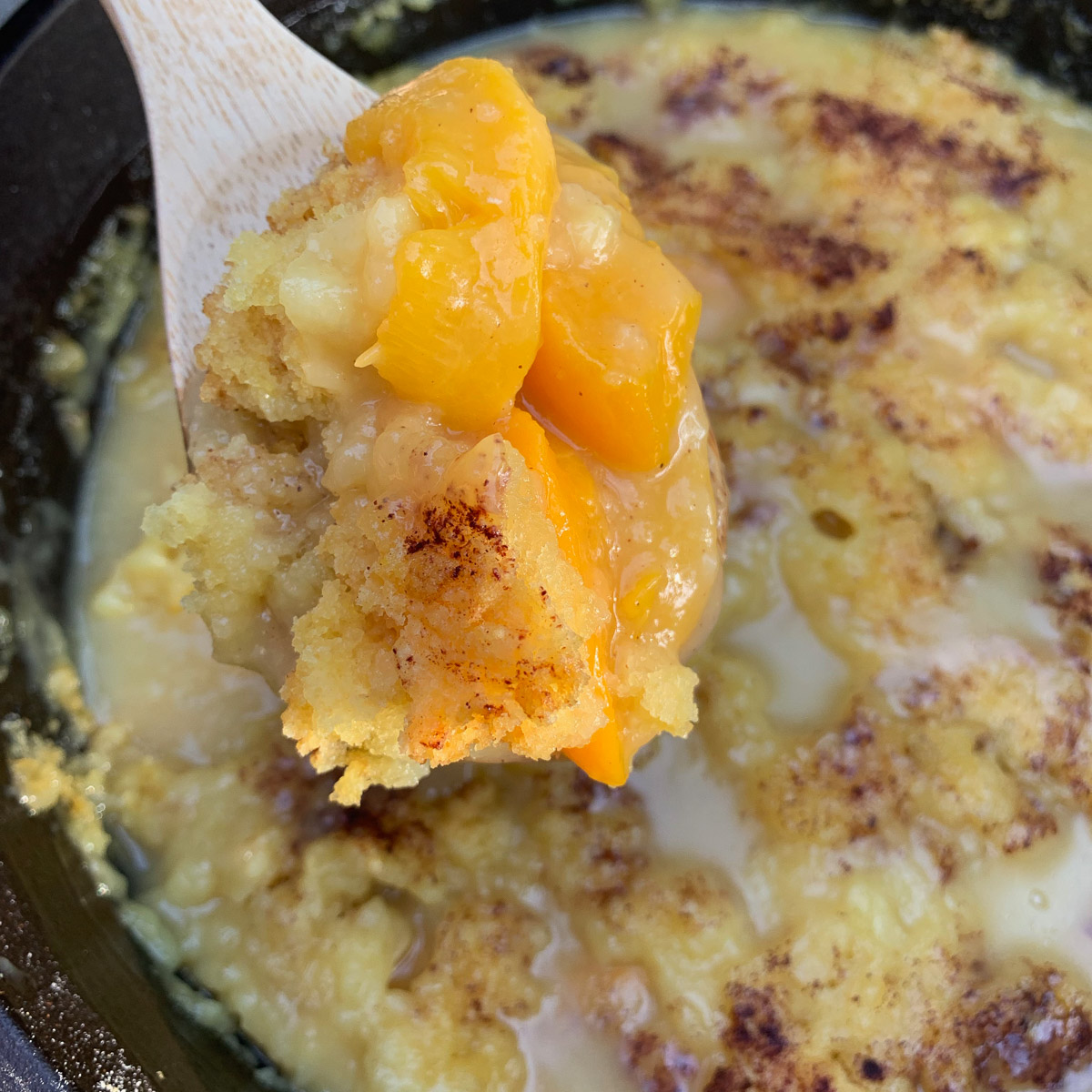 A peach dump cake with a wooden spoon lifting up a serving.