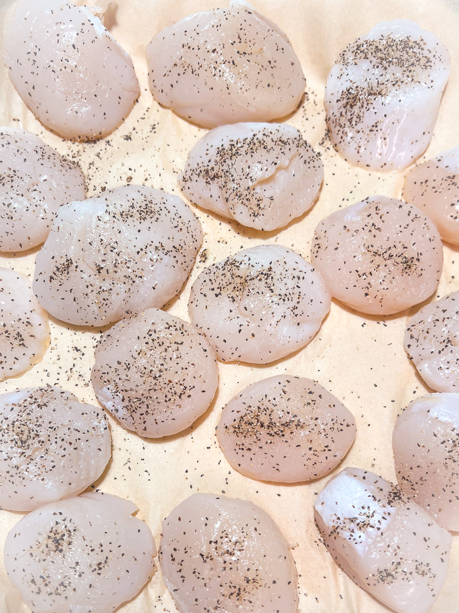 Sea scallops thawed and seasoned with salt and pepper for cooking.