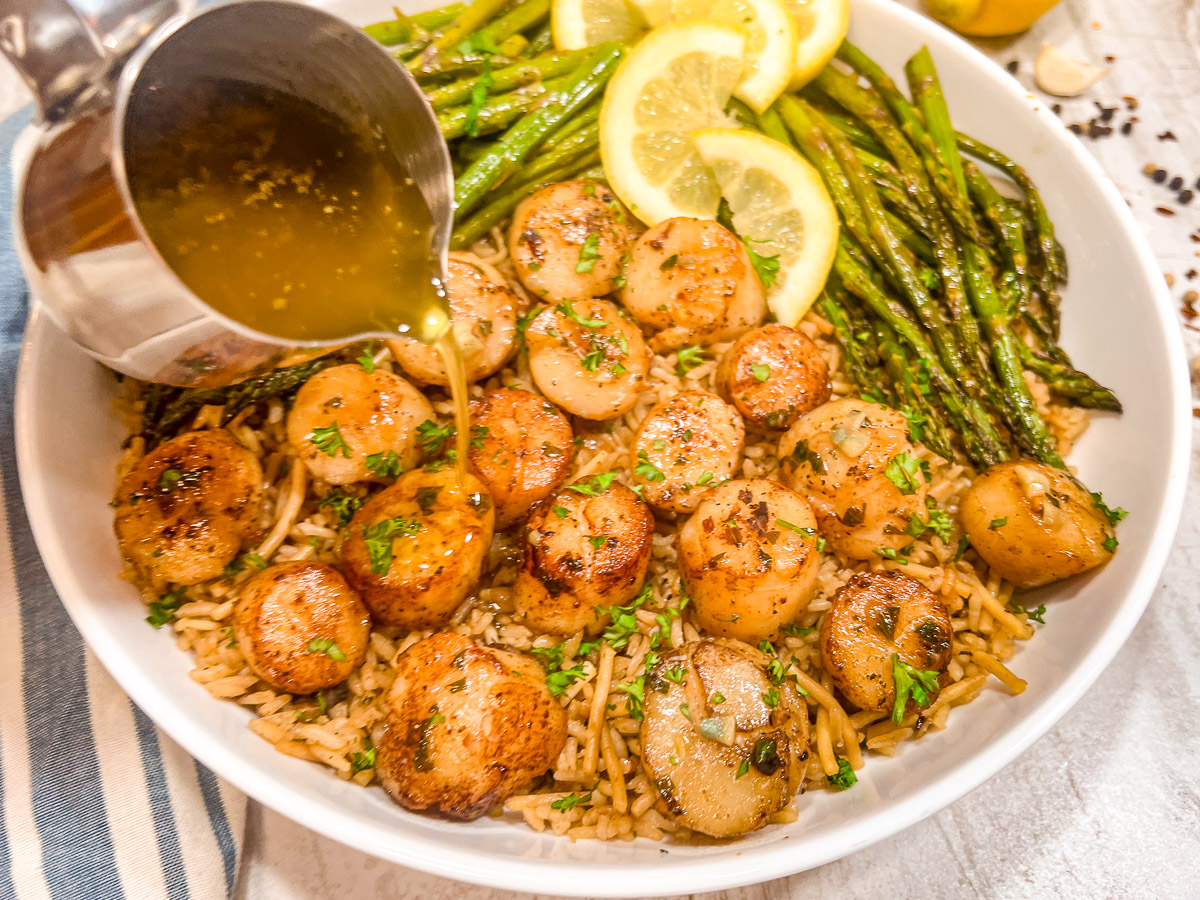 Garlic lemon butter sauce being poured over scallops.