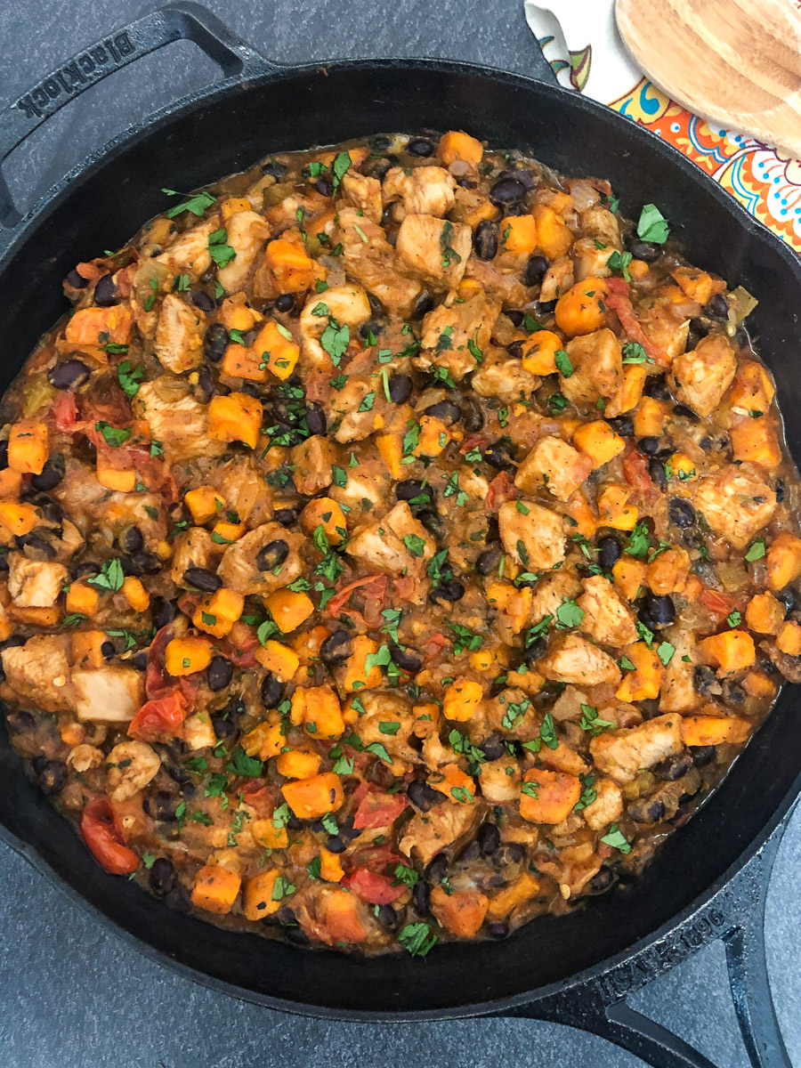 Mexican inspired skillet dinner with chicken, sweet potatoes, black beans, tomatoes, garnished with cilantro and queso fresco.
