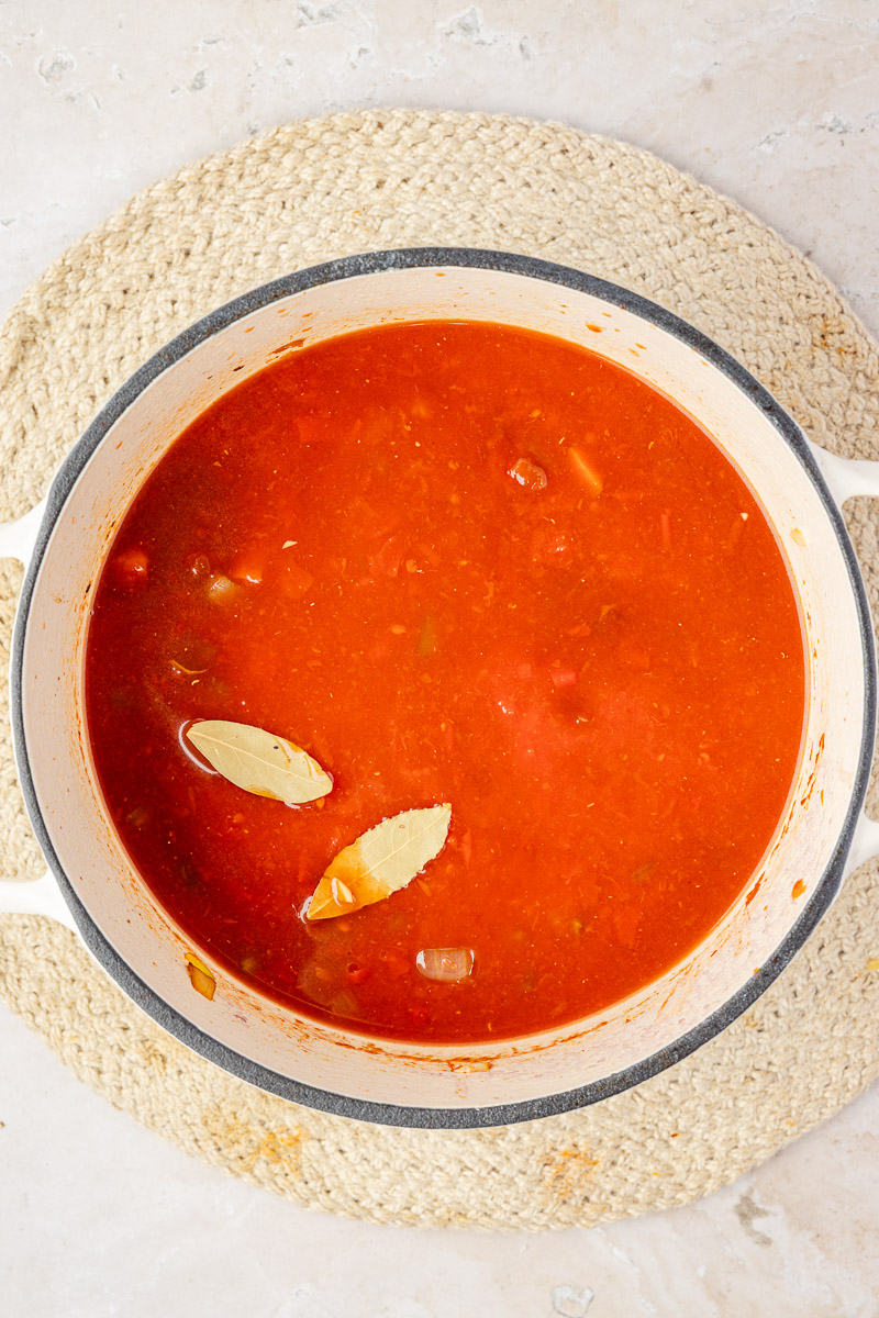 Chicken broth, crushed tomatoes, and bay leaves added to the dutch oven.