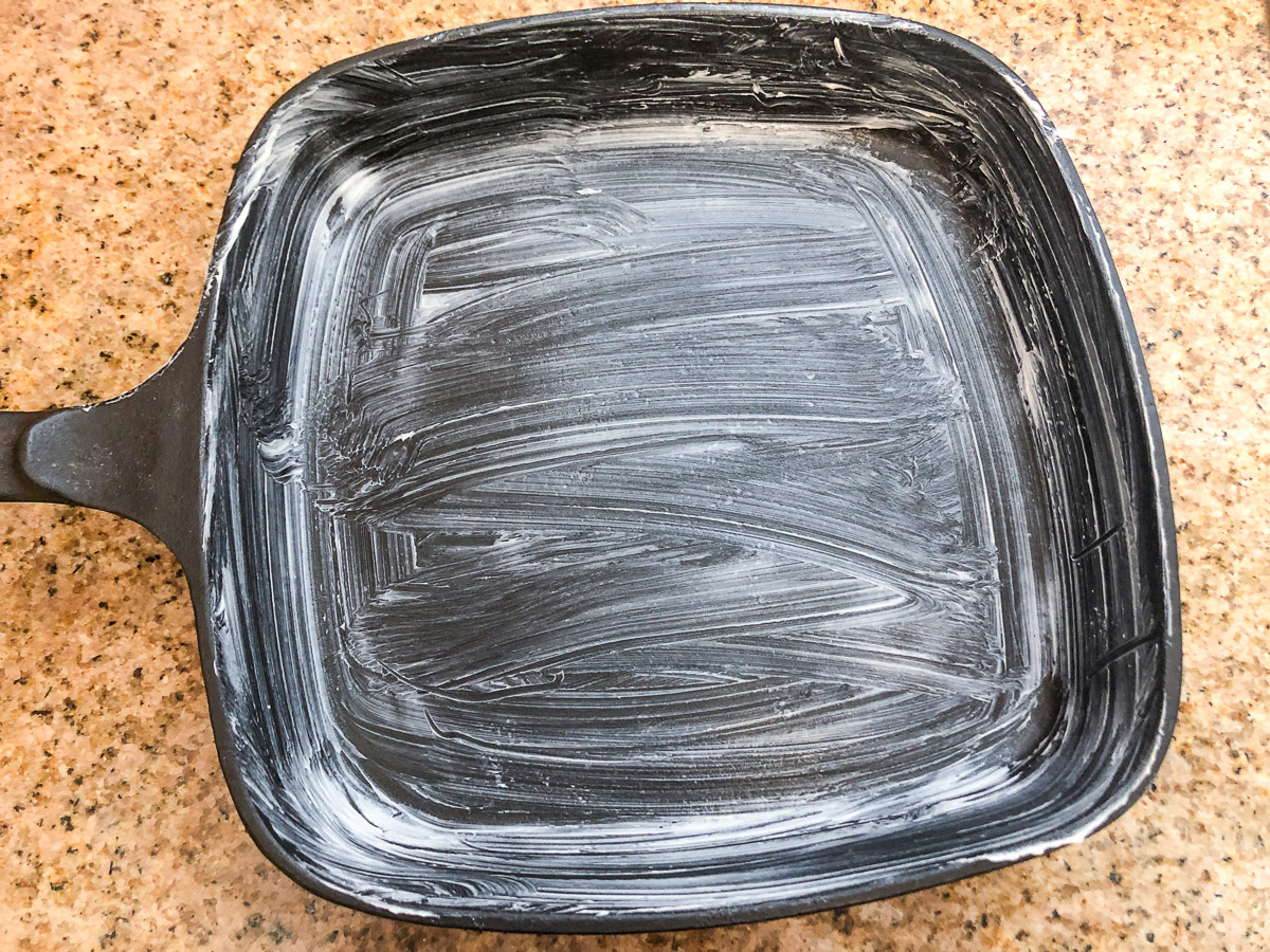 A cast iron skillet greased with butter and ready to preheat in the oven.