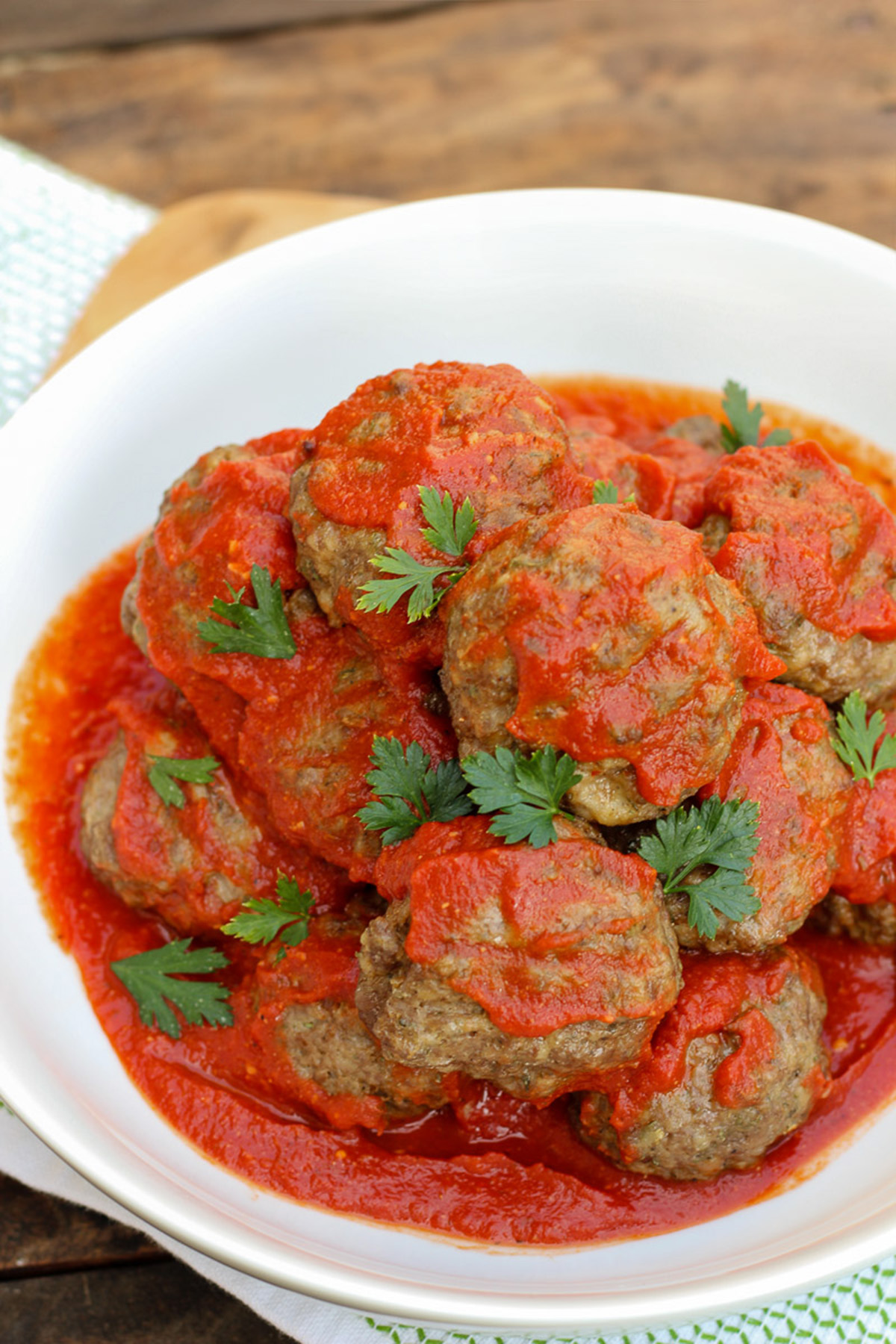 A white serving bowl full of Italian meatballs in red sauce garnished with fresh chopped parsley.