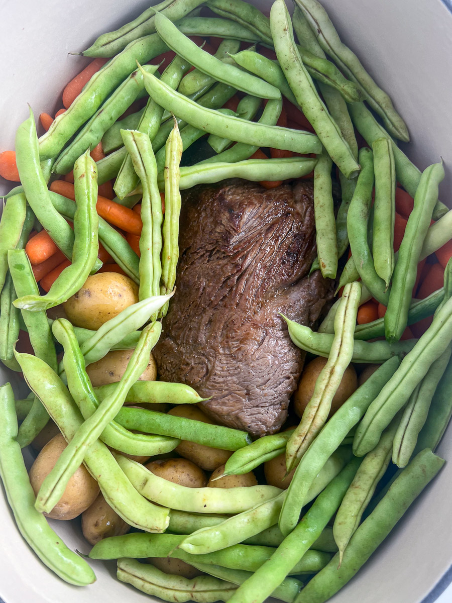 Fresh green beans have been added to the dutch oven over the carrots, potatoes, and roast.