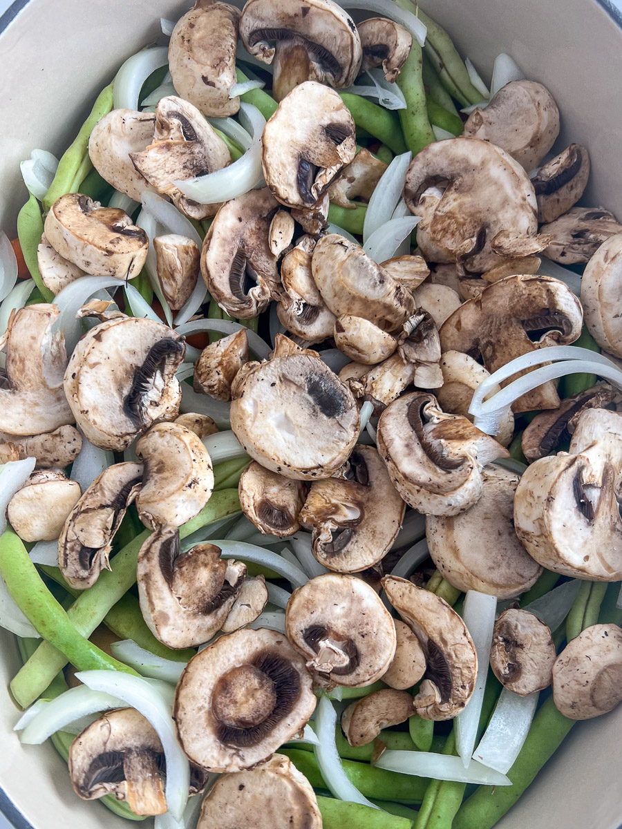 Sliced mushrooms and onions on top of everything in the dutch oven.