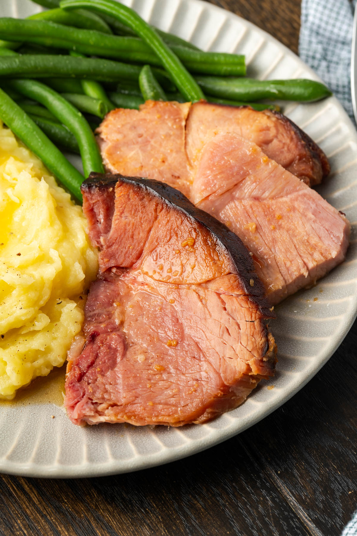 Slices of ham with a side of mashed potatoes and green beans.