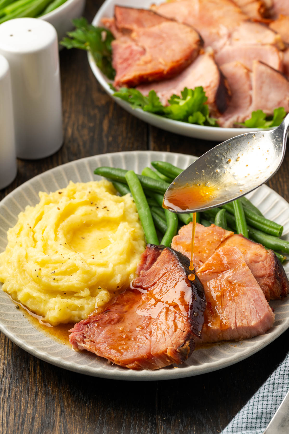 A spoon pouring the juices over a plate of Dutch Oven ham.