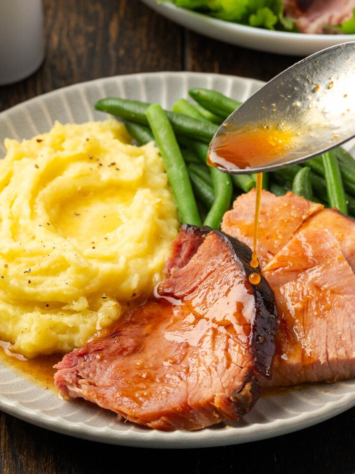 Dutch oven ham slices on a plate with spoon drizzling some glaze over the top.