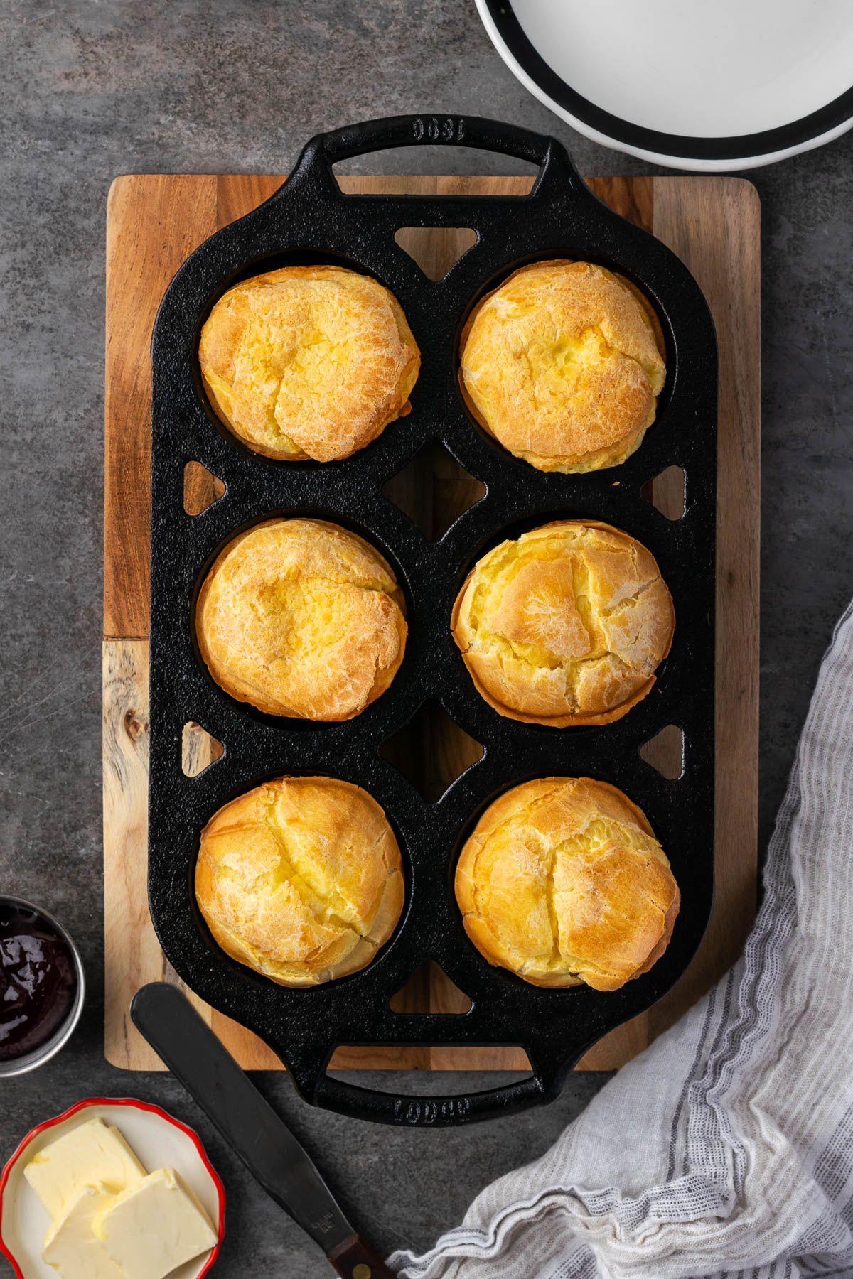 A muffin pan filled with popovers on a cutting board