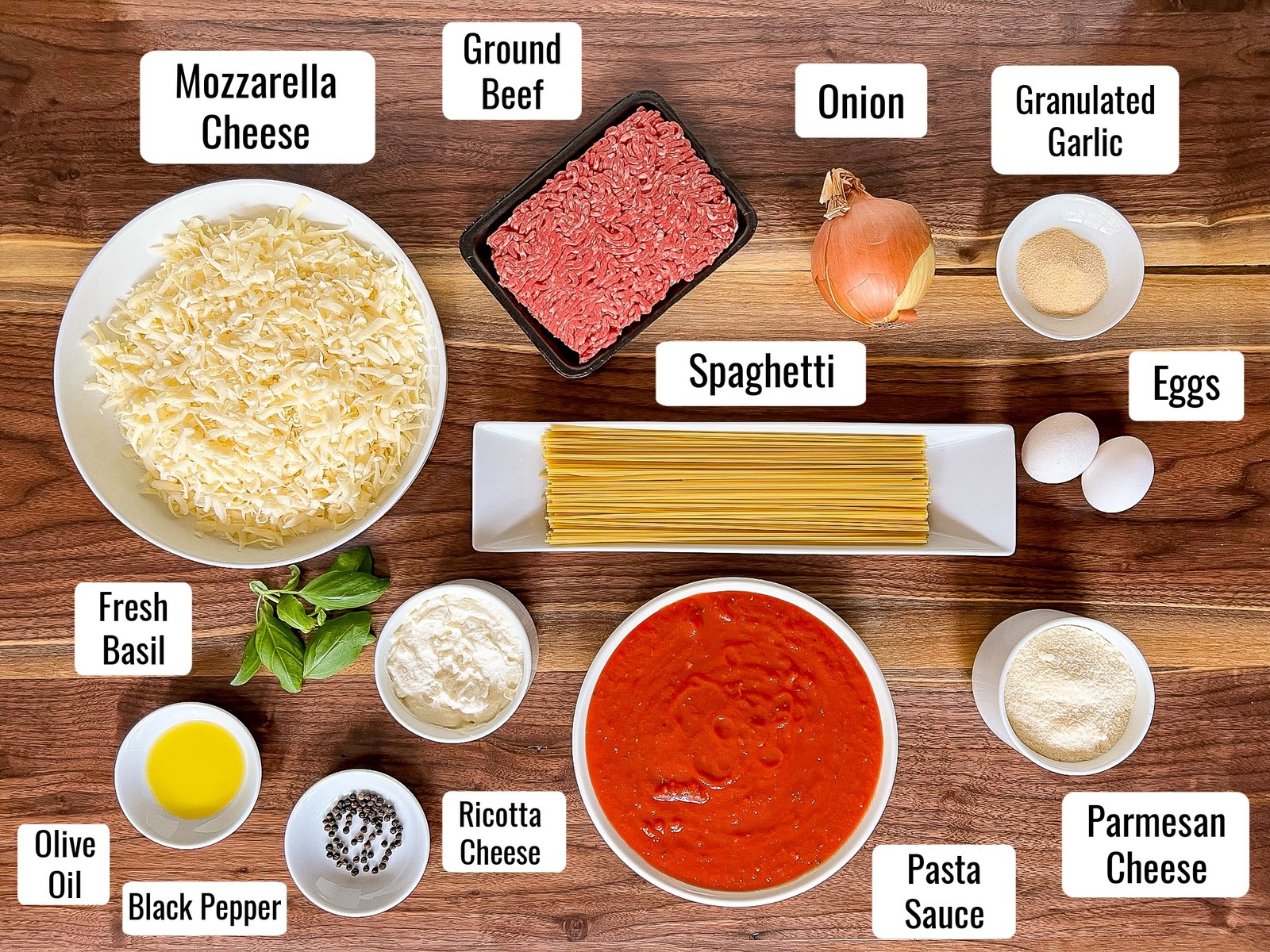 Ingredients for the recipe, mozzarella cheese, ground beef, onion, granulated garlic, spaghetti, eggs, parmesan cheese, pasta sauce, ricotta cheese, black pepper, olive oil, and fresh basil.
