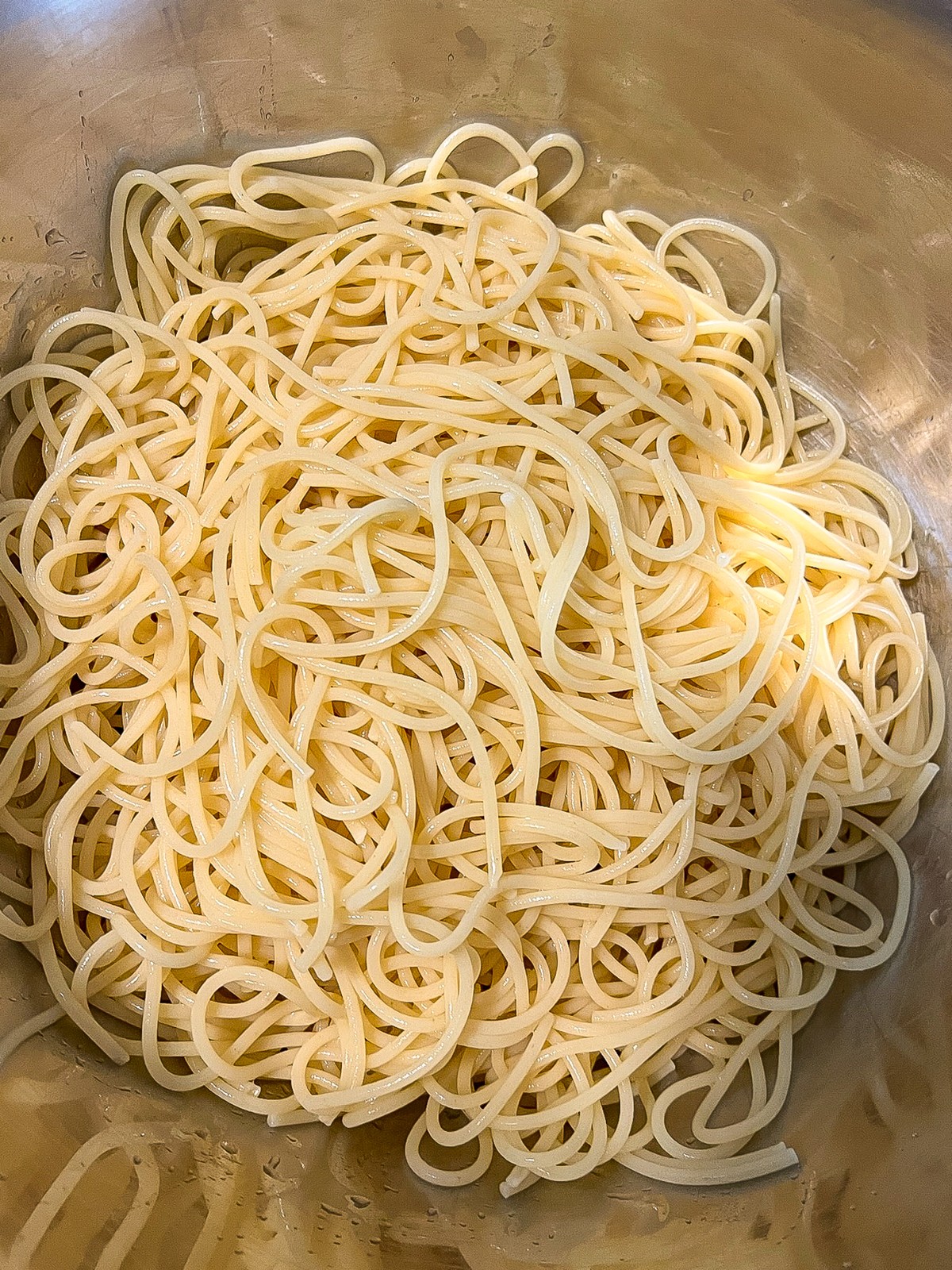 Cooked and drained spaghetti in a stainless steel bowl.