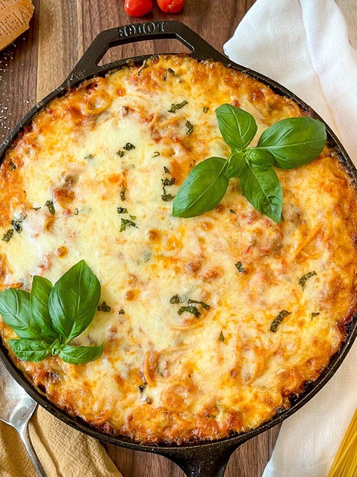 Baked Spaghetti Casserole in a cast iron skillet garnished with fresh basil.