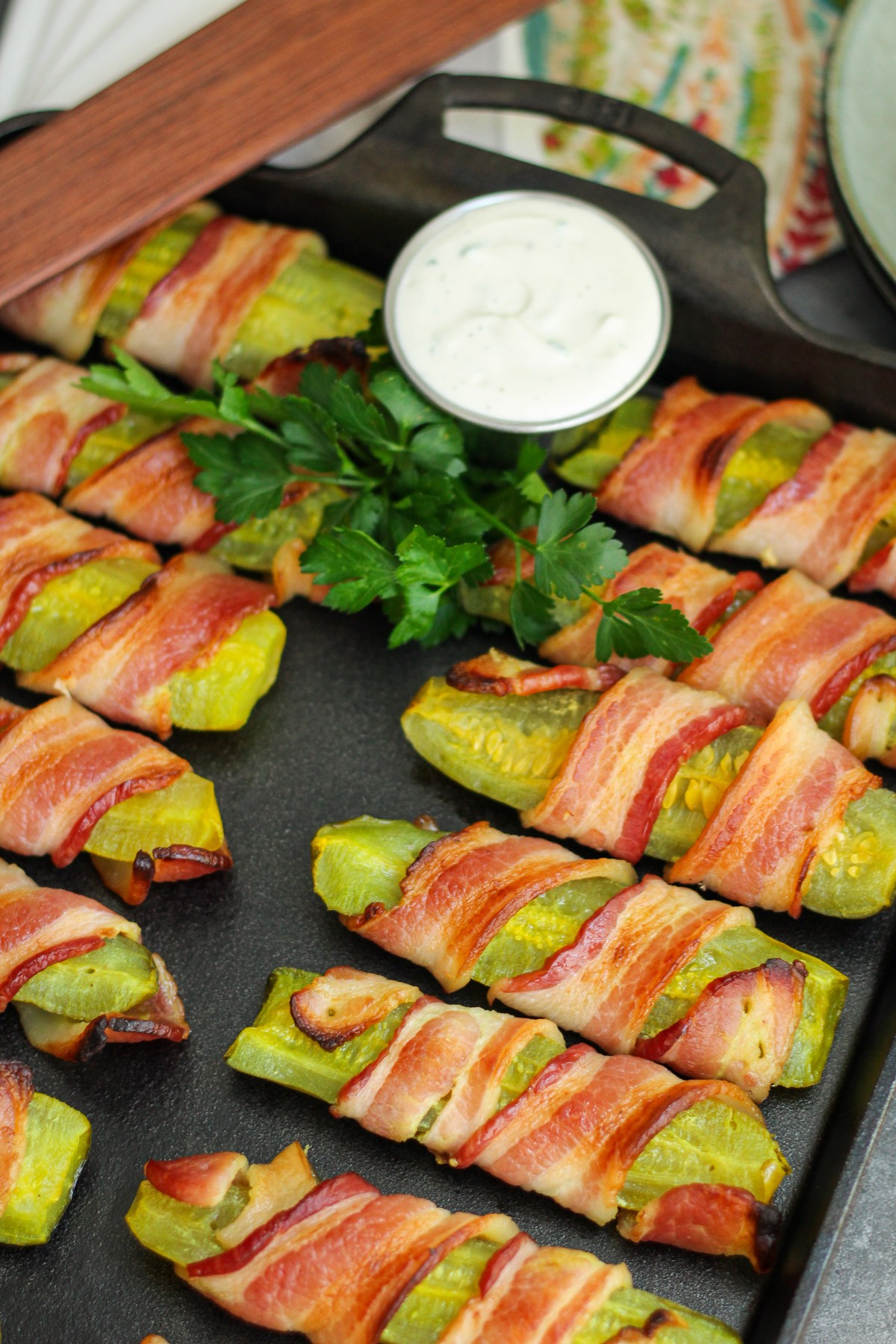 Bacon wrapped pickles on a cast iron baking tray with ranch for dipping.