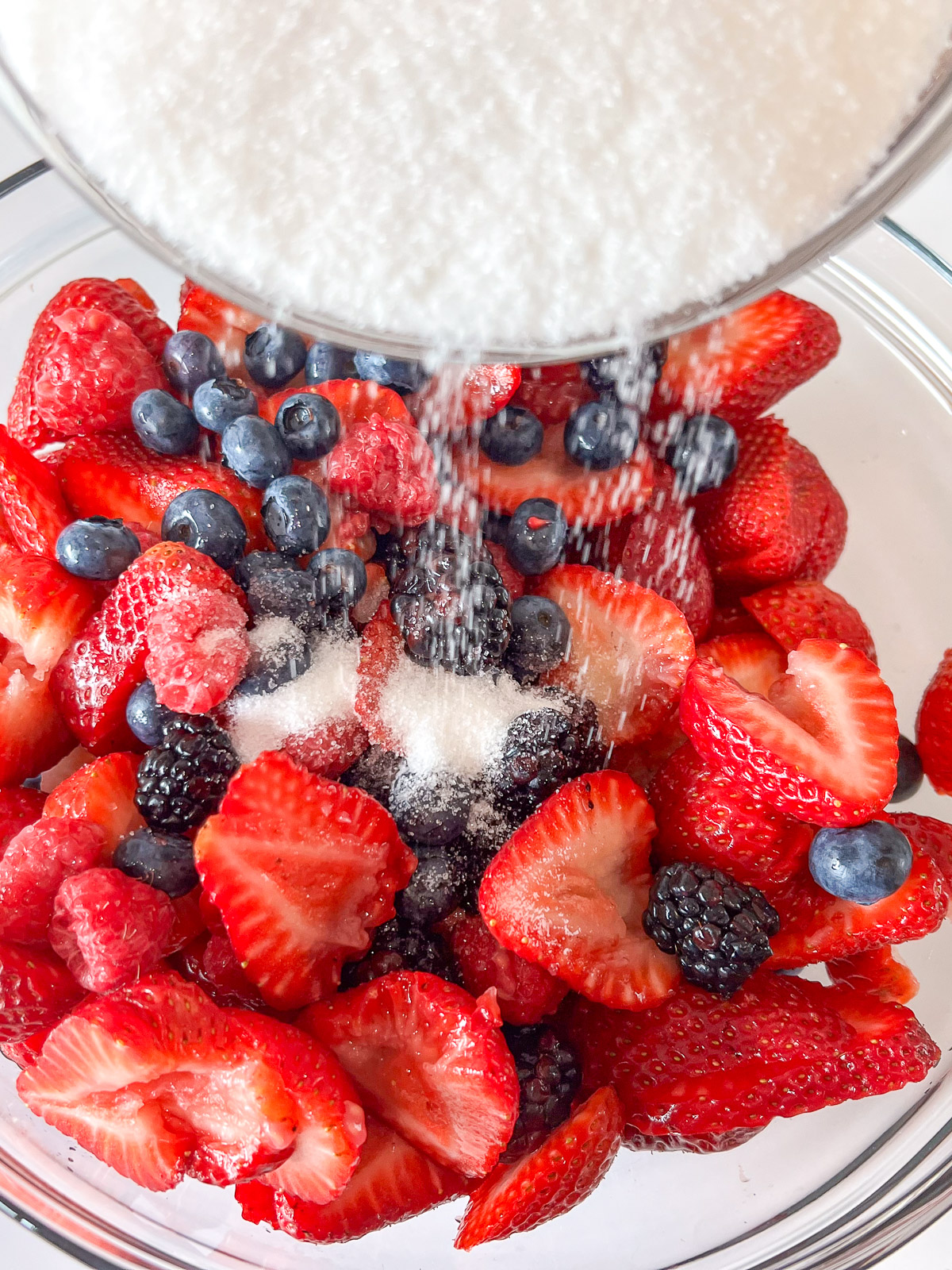 Mixed berries in a bowl being tossed with sugar for cast iron skillet berry cobbler