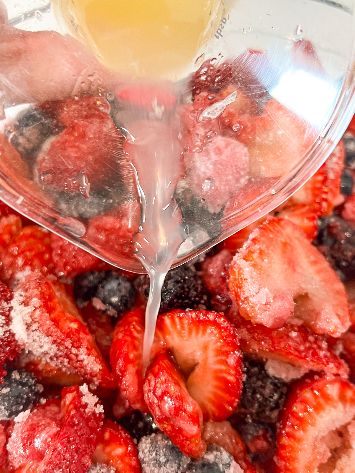 Lemon juice being poured over sugared berries for berry cobbler maceration