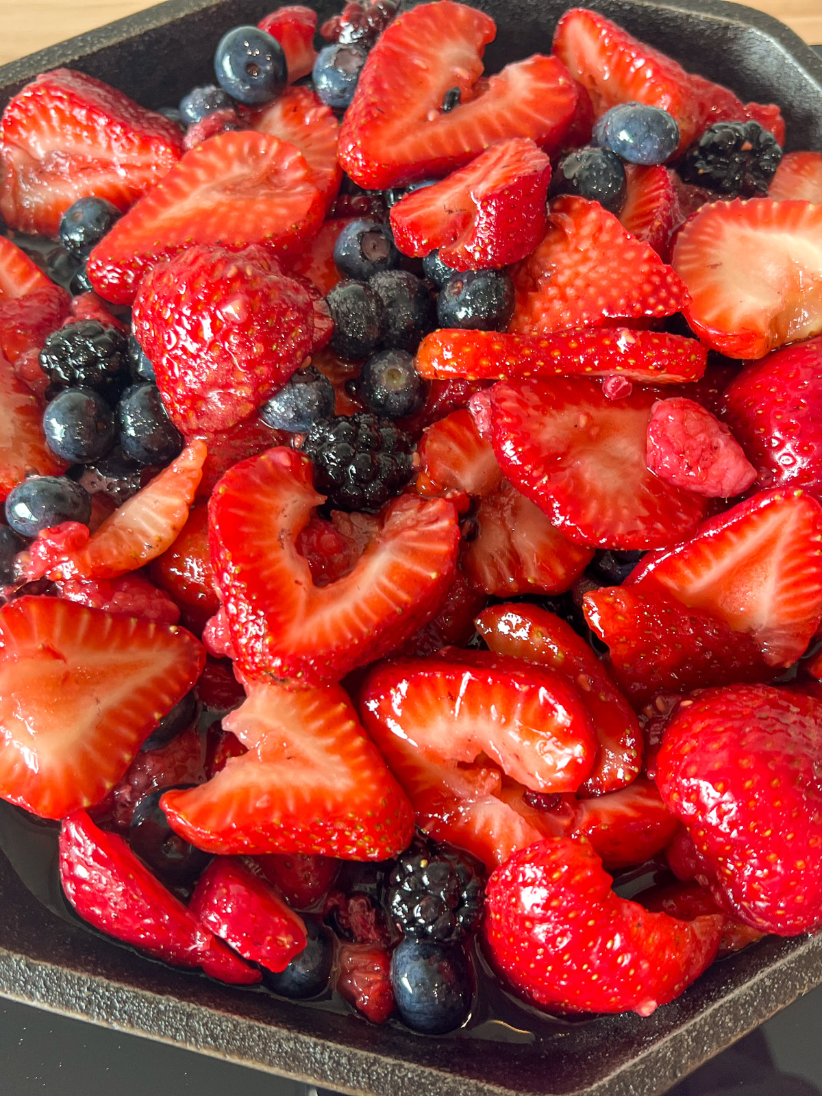 Mixed berries cooking down in a cast iron skillet turning deep purple