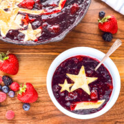 Bowl of cast iron skillet berry cobbler topped with a golden pie crust star served with fresh mixed berries